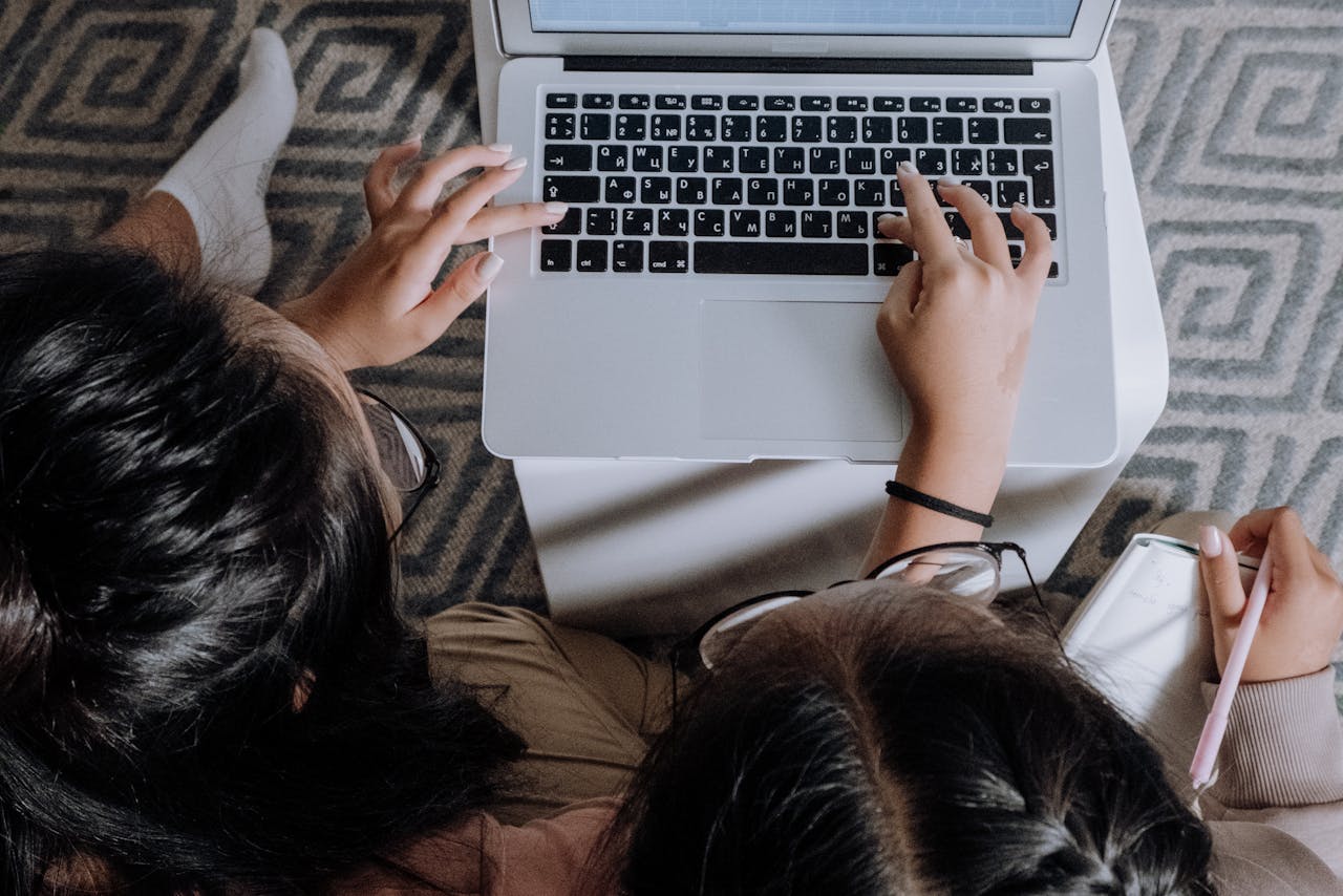 Two teenage girls sitting together at home, focused on a laptop